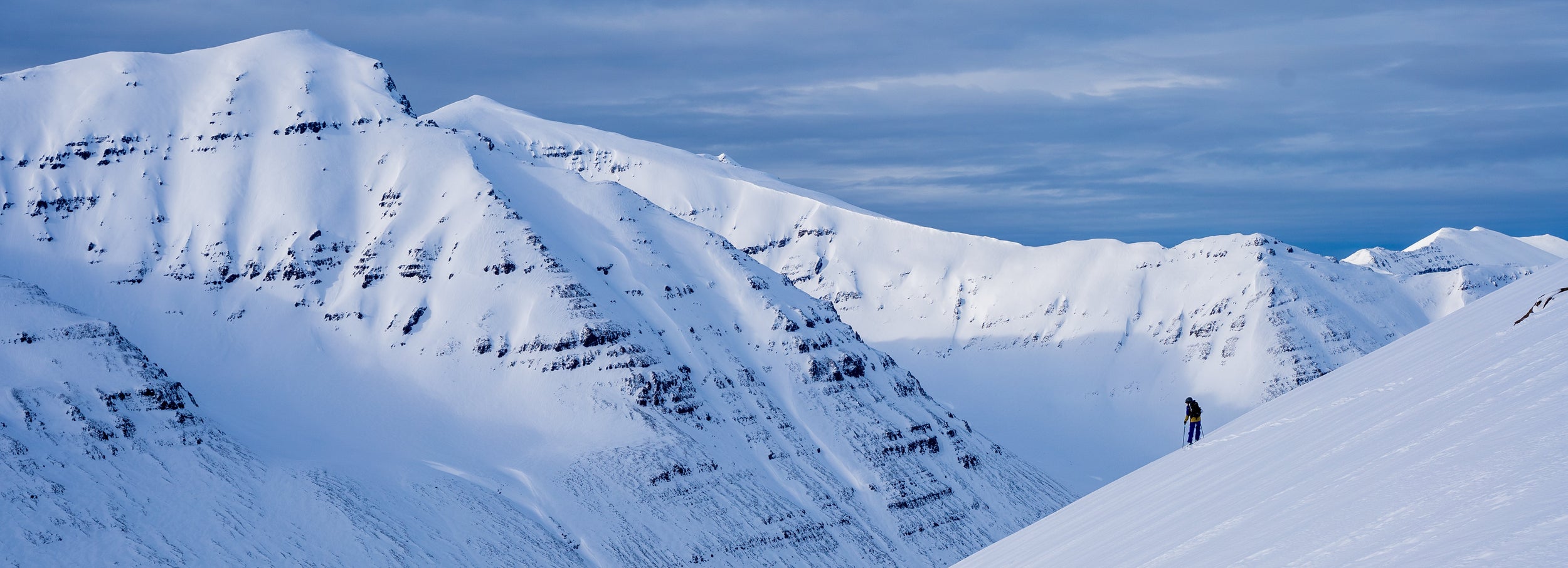 Backcountry skier standing on a snow-covered mountain with a vast landscape in the background in Iceland.