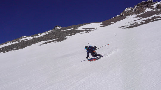 A skier arcing a turn above his guide on Mt Shasta